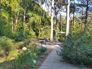 A pathway leading to a seating area with chairs and a table, surrounded by dense greenery and trees.
