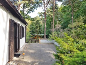 A pathway leading to a building with a white exterior and dark shutters, surrounded by dense greenery and trees.