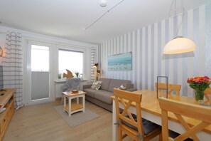 Un salon moderne avec un canapé, une table basse et une table à manger. Les murs sont rayés et il y a une grande fenêtre.