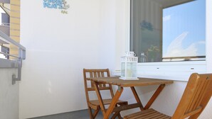 Un tavolino in legno con due sedie, una lanterna bianca e una finestra con vista su una barca a vela.