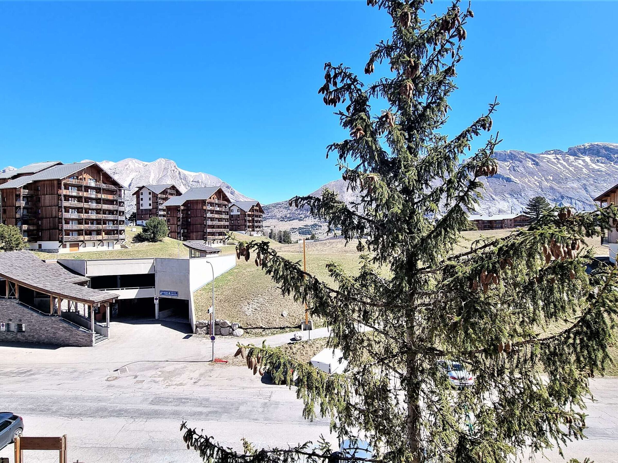 Un complejo turístico de montaña con edificios de madera, un estacionamiento y vistas de montañas nevadas.