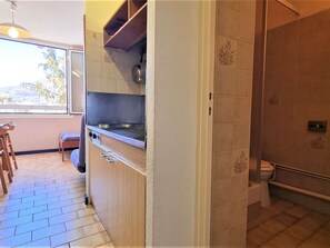 Compact kitchen with stove and adjacent bathroom featuring a shower and toilet.
