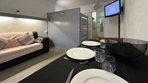 A modern room with a sofa, dining table set with plates and glasses, a TV mounted on the wall, and a grey partition. - Comfortable studio for 4 with terrace, parking, wifi and pets allowed (Le Dévoluy)