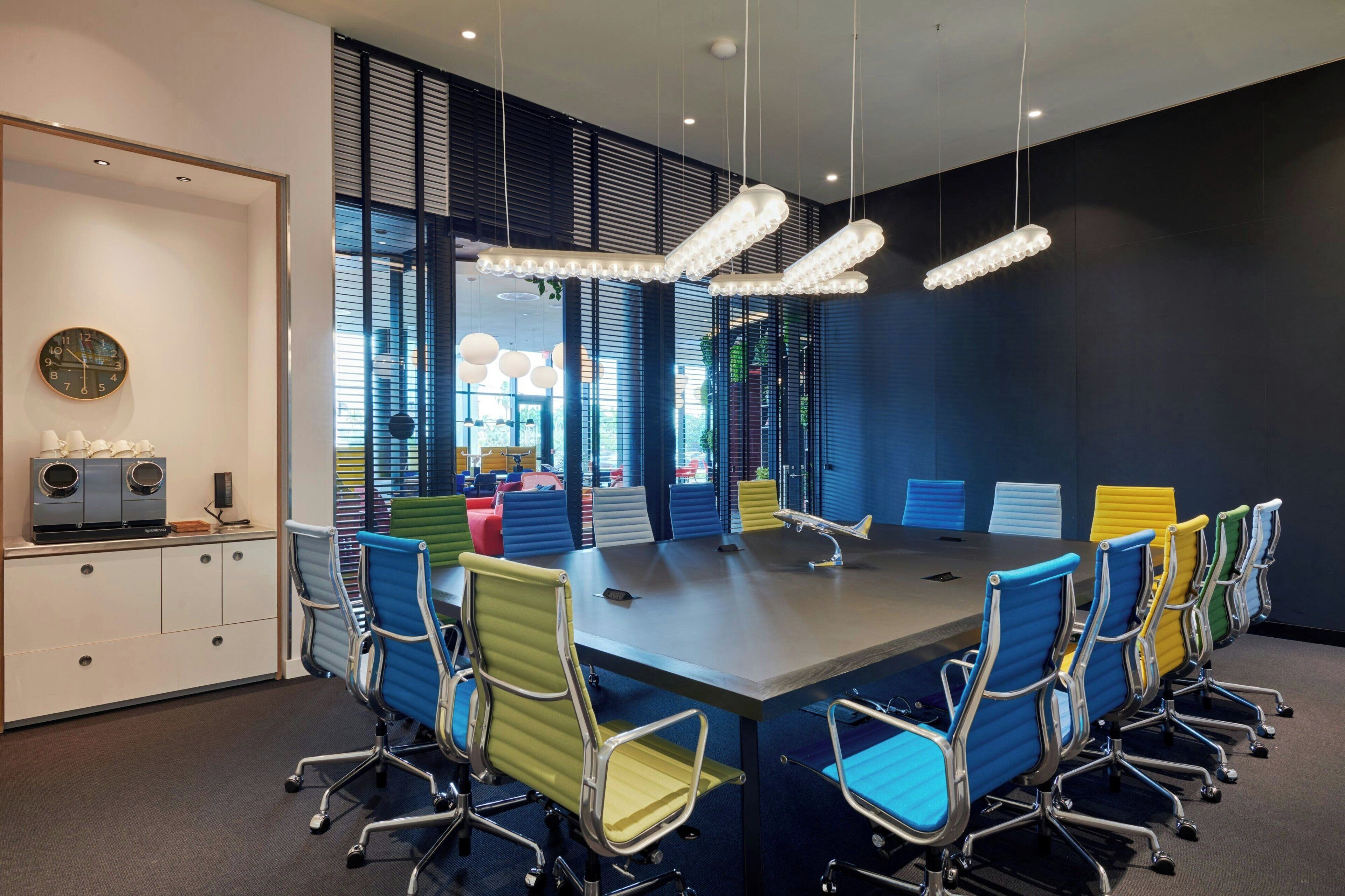 Une salle de conférence dotée d’une longue table, de chaises aux couleurs vives et d’un lustre moderne.