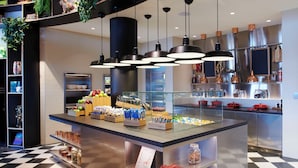 A modern kitchen with a central island, black and white checkered floor, hanging plants, and various kitchen appliances. - citizenM Miami Worldcenter (Miami)