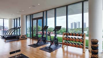 Un gimnasio espacioso con cintas de correr, bicicletas estáticas y un estante con mancuernas.