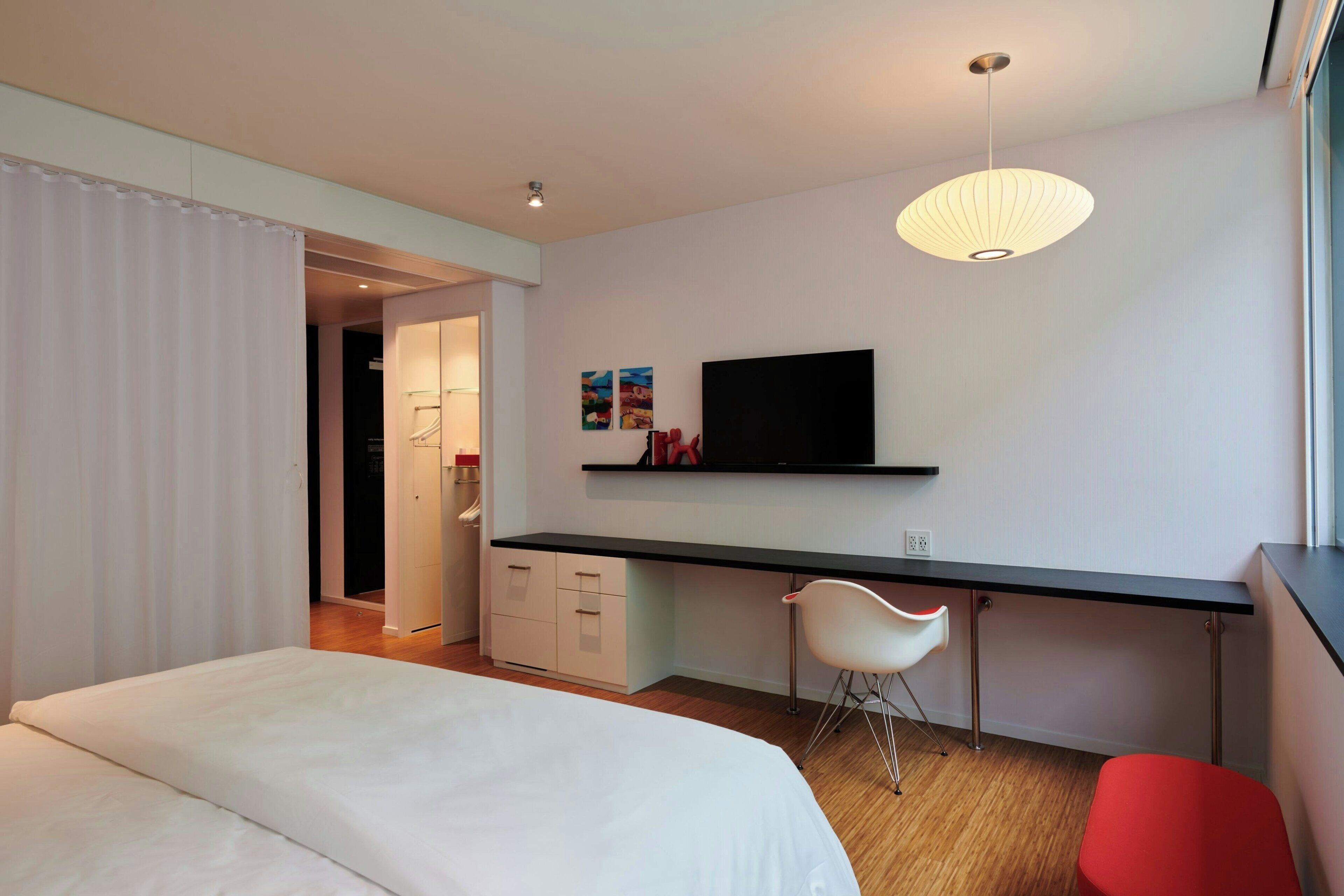 Une chambre d’hôtel moderne équipée d’un lit, d’un bureau avec une chaise, d’une télévision et d’une fenêtre.