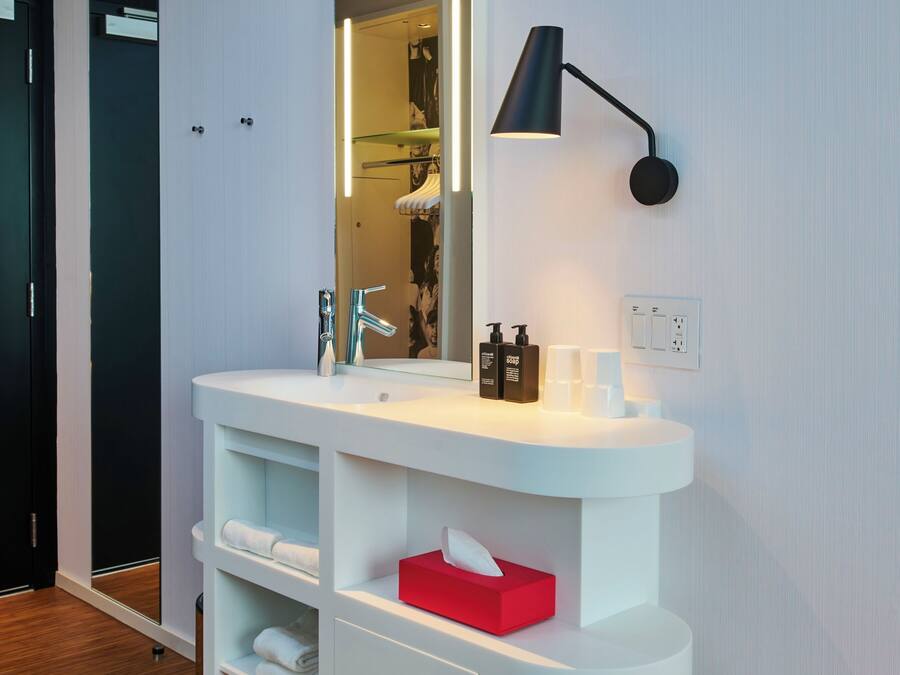 Un baño moderno con tocador blanco, un espejo y un taburete rojo.