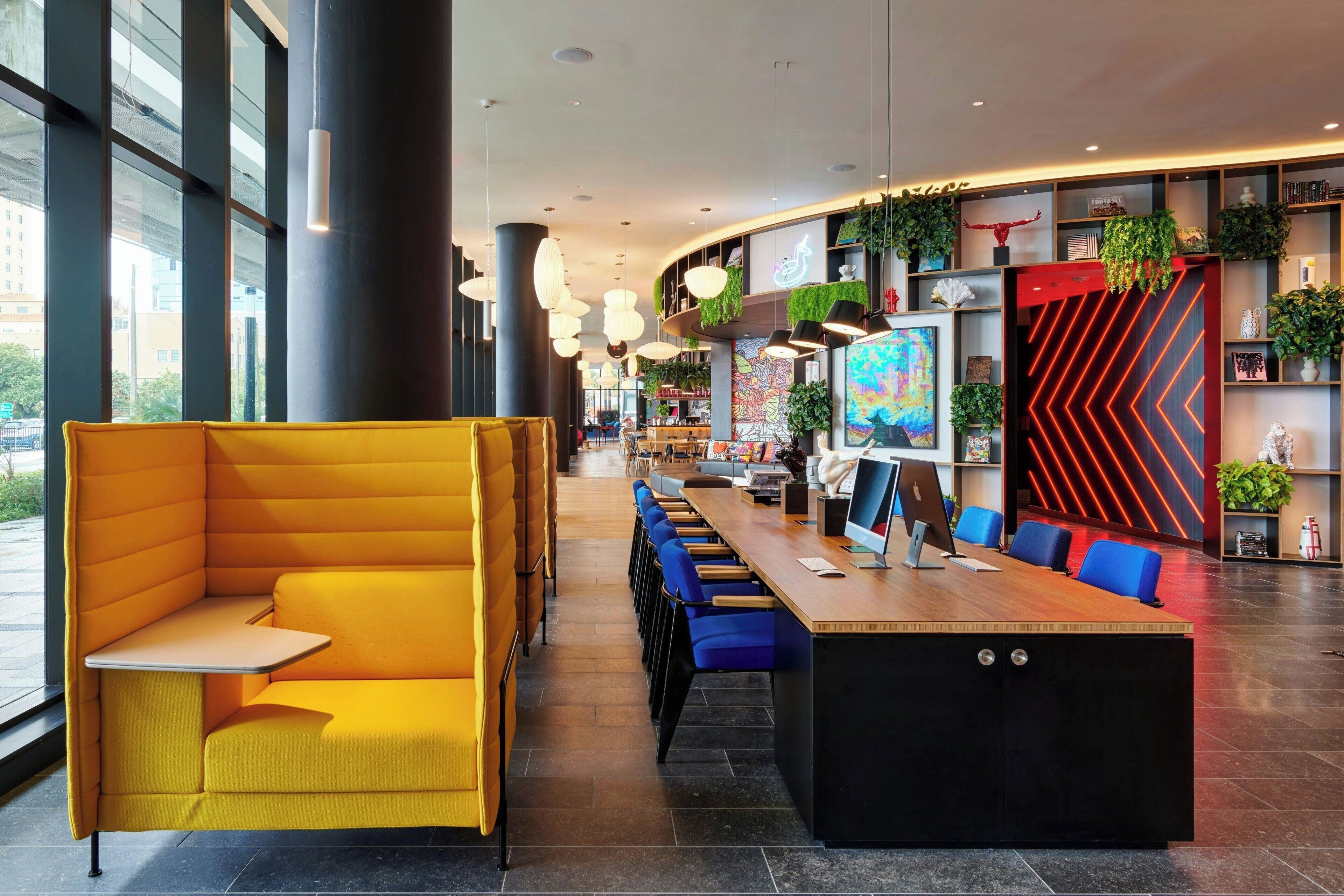 Un intérieur moderne avec des banquettes jaunes, une longue table avec des chaises bleues et une grande fenêtre.