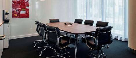A conference room with a round table, black office chairs, and a red abstract art piece on the wall.