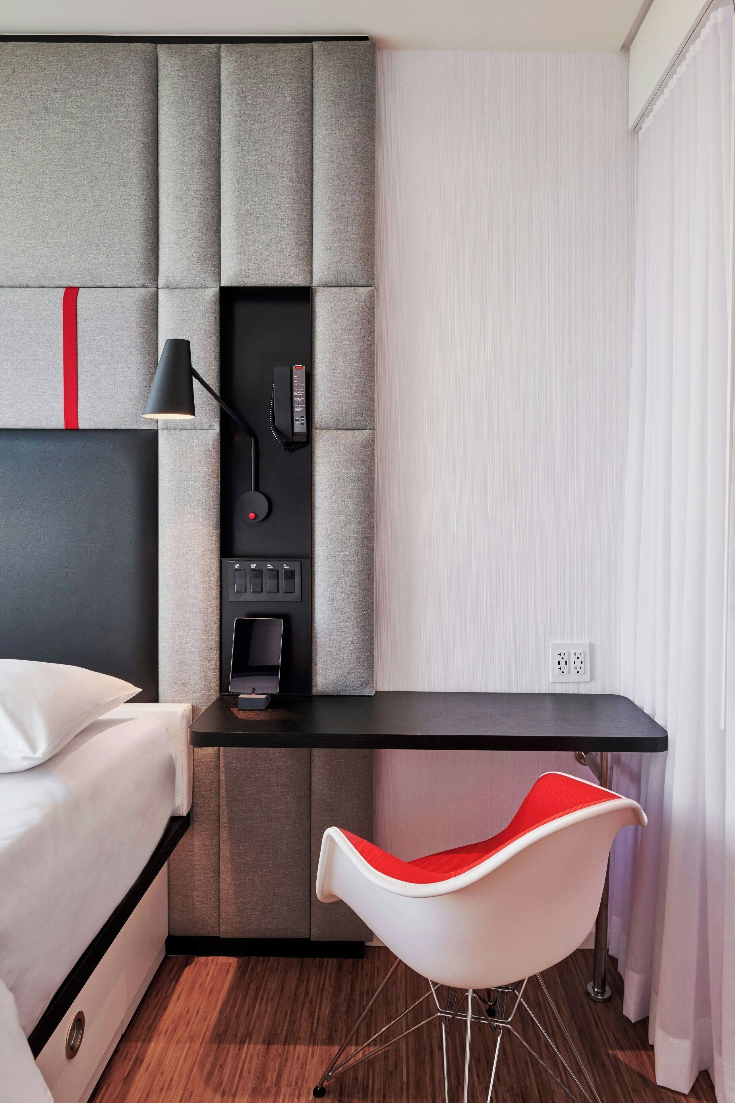Una habitación de hotel moderna con una cama, un escritorio con una silla, un teléfono y un panel de control.