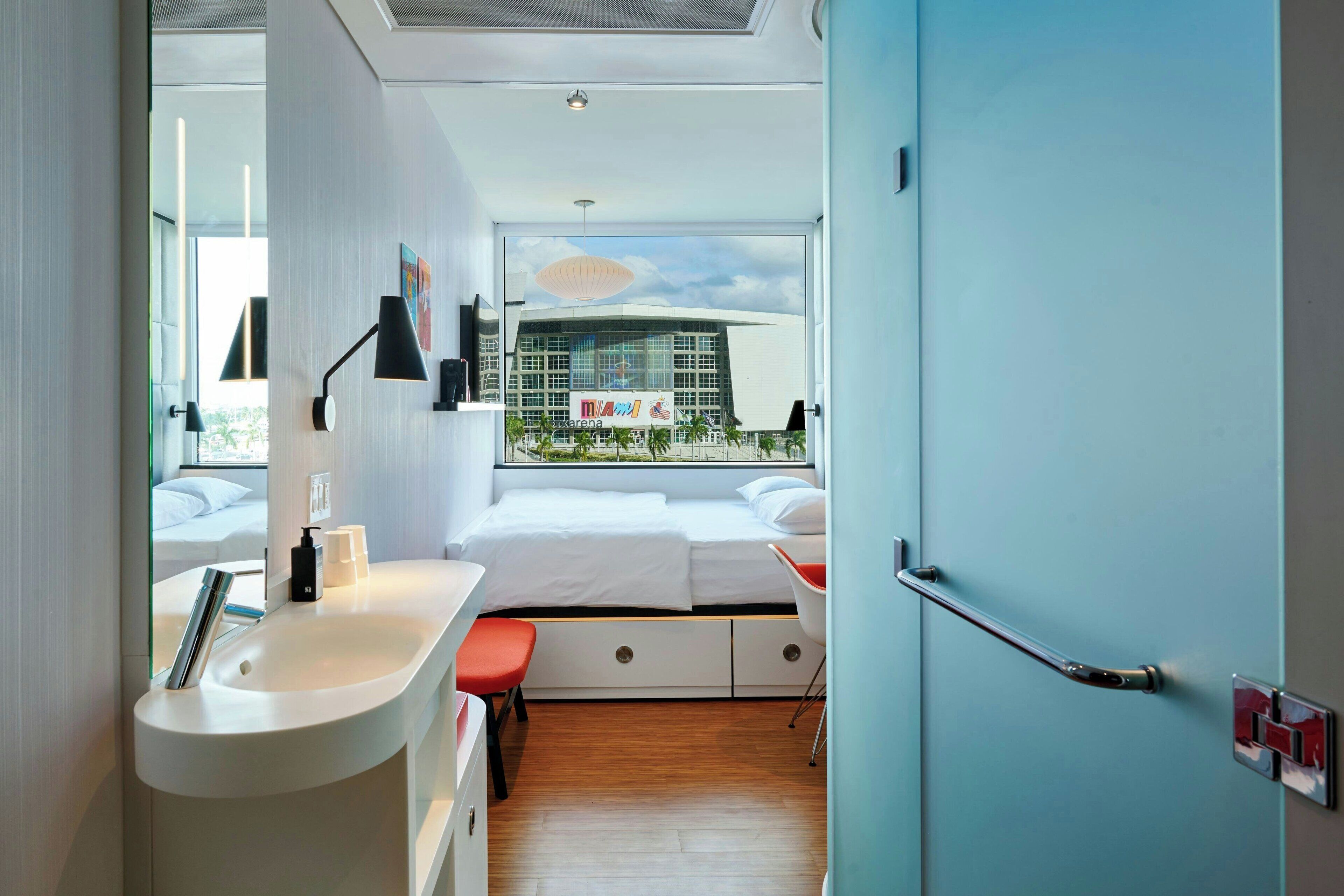 Habitación de hotel moderna con cama, un lavamanos blanco, una silla roja y vista a un edificio.