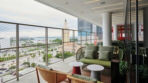 A balcony with wicker chairs and a sofa, overlooking a cityscape with a prominent tower. - citizenM Miami Worldcenter (Miami)