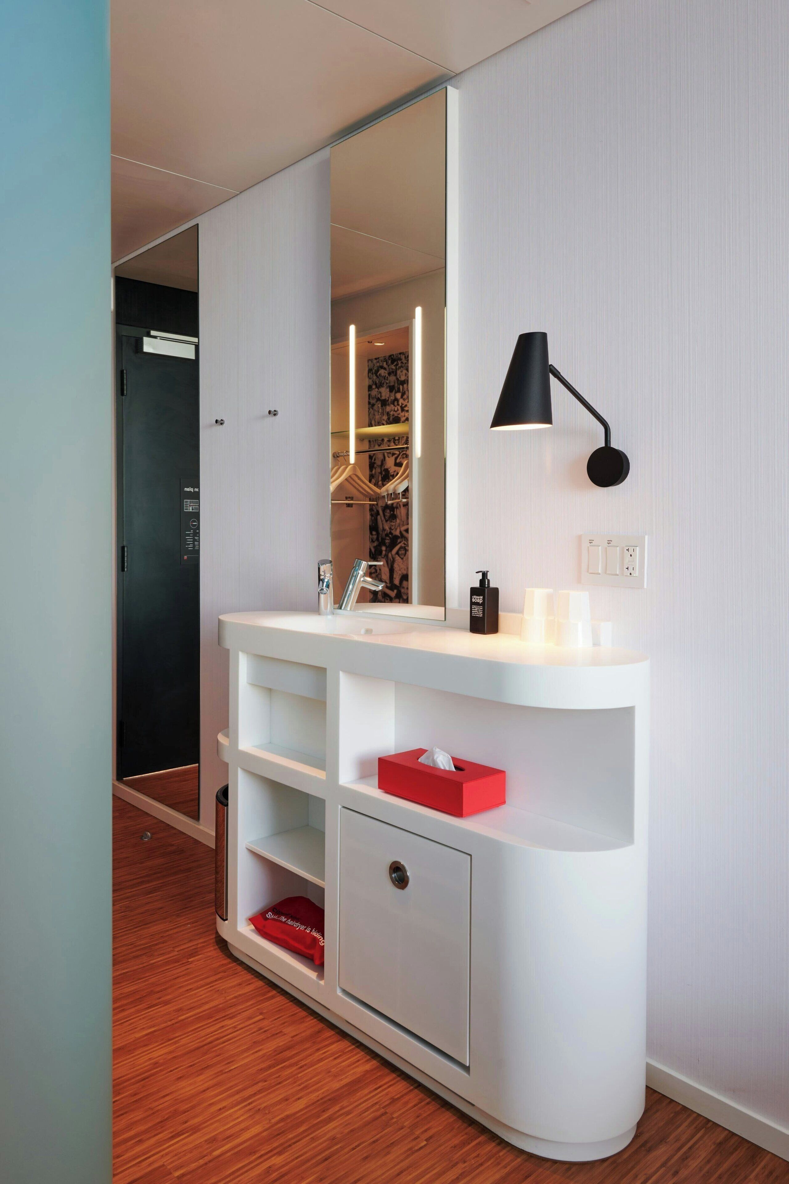 Une salle de bain moderne avec un meuble-lavabo blanc, une lampe murale noire et un porte-mouchoirs rouge.