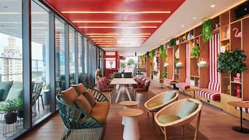 A modern lounge area with wicker furniture, a central table, and a view of the cityscape through large windows.