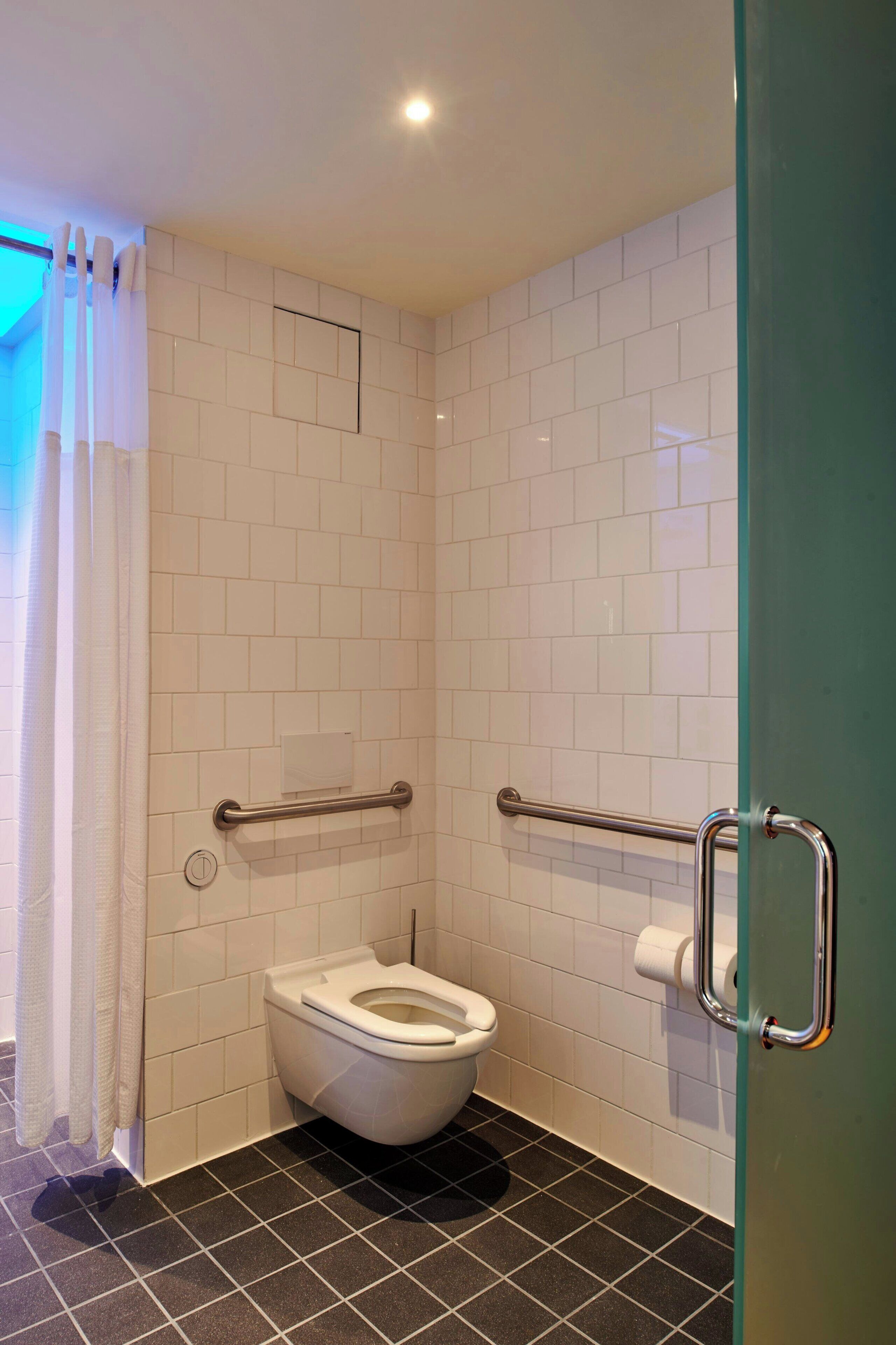 Ein kleines, modernes Badezimmer mit weißen Fliesen, einer weißen Toilette und einer Duschkabine aus Glas.