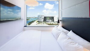 A modern hotel room with a large window, a bed, and a view of a coastal area with a bridge and a building labeled "Korea Mall". - citizenM Miami Worldcenter (Miami)
