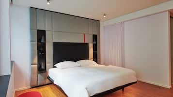 A modern hotel room with a large bed, built-in shelving, and a red accent wall.