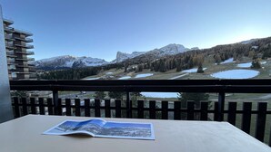 A balcony with a view of snow-capped mountains, a lake, and a building in the background.