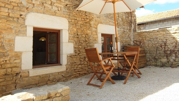 A stone building with a patio area featuring a table and chairs, an umbrella, and a bottle of wine.