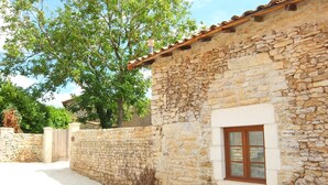 A stone building with a wooden door and window, surrounded by a gravel driveway and a stone wall.