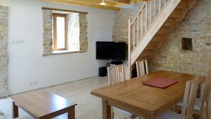 A room with a wooden dining table, chairs, a TV, and a stone wall.