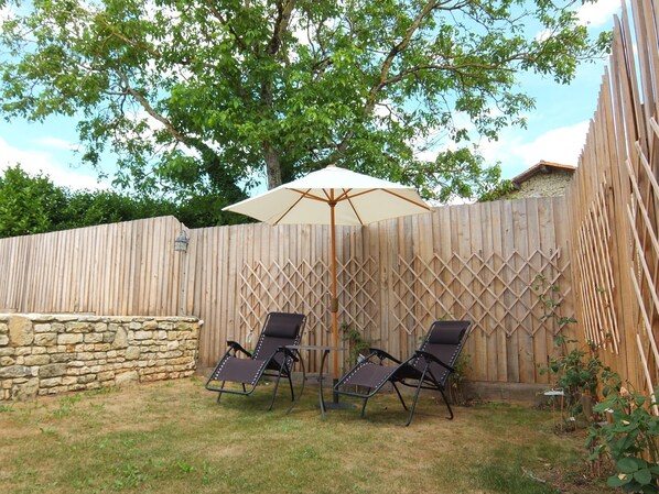 A backyard with a wooden fence, two lounge chairs, a table, and an umbrella. - Old Atelier Gite: 4-Star Old Stone Cottage with Private Garden and Free Wi-Fi (La Chèvrerie)