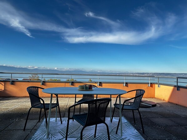 A terrace with a round table and four chairs, overlooking a cityscape and a body of water.