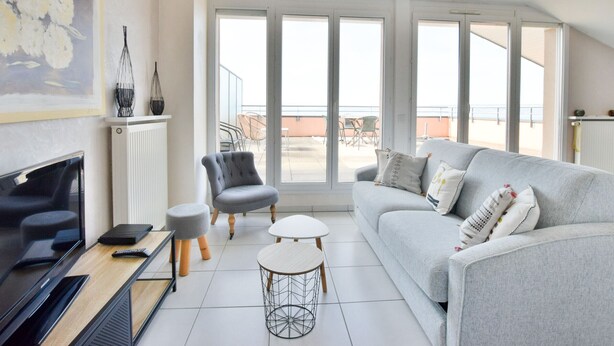 A modern living room with a grey sofa, a television, and a dining table.