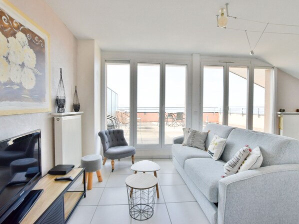 A modern living room with a grey sofa, a television, and a dining table.
