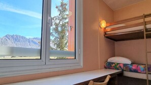 A bunk bed with a colorful mattress, a desk with a chair, and a window with a view of mountains.