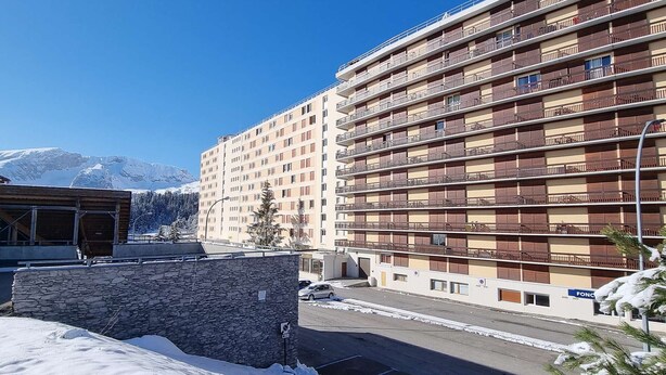A multi-story hotel with balconies, a parking area, and a mountainous backdrop.
