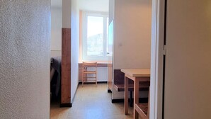 A narrow hallway with a radiator, a window with a view of a mountain, and a wooden table with chairs.