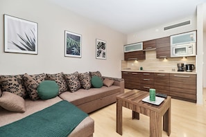 A modern living room with a sofa, a coffee table, and a kitchen area with cabinets and appliances.