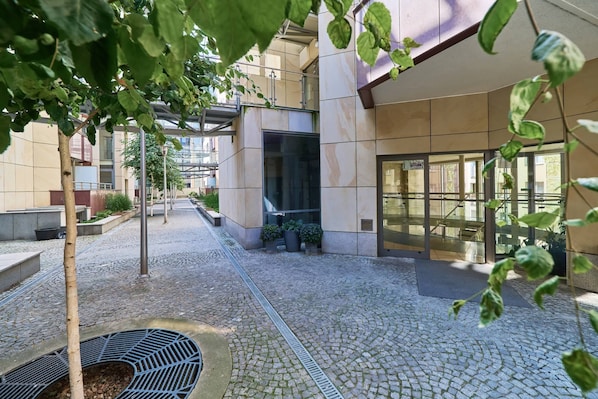 A courtyard with cobblestone flooring, potted plants, and a building entrance with large windows.