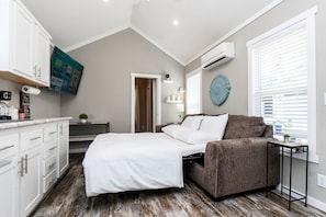 A bedroom with a bed, a brown sofa, a small table, a TV, and a window with blinds. - - Adorable Guest House in South Tyler - (Tyler)