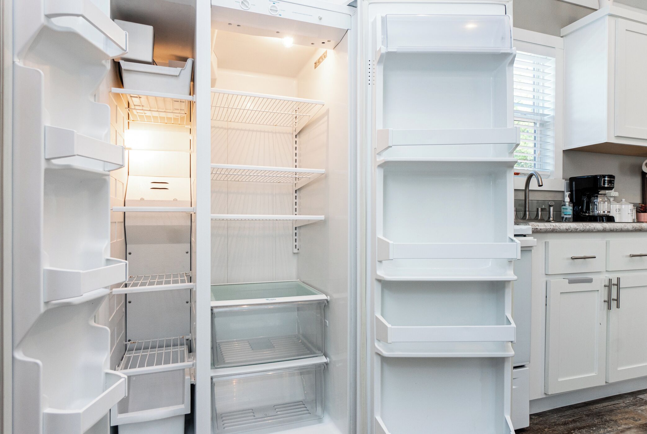 Een moderne keuken met witte kasten, een inbouwkoelkast en een koffiezetapparaat op het aanrecht.