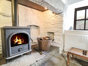 A stone fireplace with a modern wood-burning stove, a wicker basket with logs, and a wooden table with a cup.