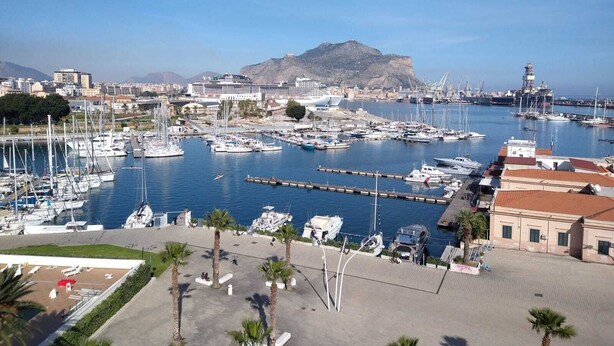 Un port de plaisance où sont amarrés de nombreux bateaux, un grand navire de croisière et, au loin, une montagne imposante.