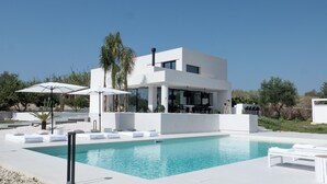 Ein modernes, zweistöckiges Haus mit Swimmingpool, Sitzgelegenheiten im Freien und einer Terrassenfläche.