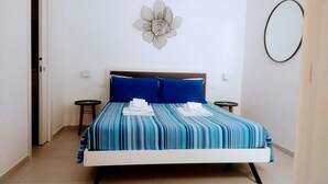 Una cama bien hecha con ropa de cama a rayas azules y blancas, dos almohadas y toallas dobladas sobre un cabecero blanco.