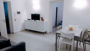 Una sala moderna con un sofá blanco, una mesa de comedor con sillas, un mueble blanco con un televisor y una pequeña estatua.