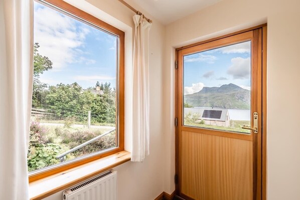 A room with a large window and a door, offering views of a mountainous landscape and a building with solar panels.
