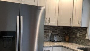 Una cocina con alacenas blancas, refrigerador de acero inoxidable, tostadora y salpicadero de azulejos.