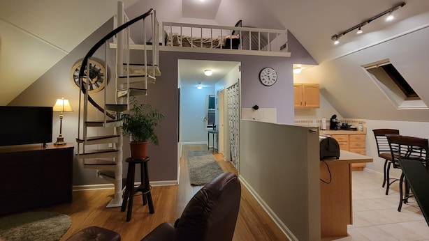 A modern loft apartment with a staircase leading to a lofted sleeping area, a kitchen with a skylight, and a dining area.