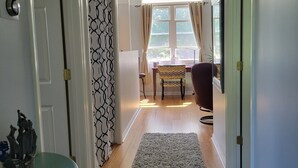A hallway with a wooden floor, a grey carpet, and a window with curtains.