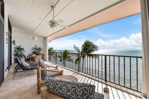 Een balkon met uitzicht op de oceaan, ingericht met gestreepte banken en stoelen, een tafel en potplanten.