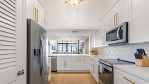 A modern kitchen with white cabinetry, stainless steel appliances, and a wooden floor. - GOOD VISIBILITY ~ 4 Bedroom, 3 Bathroom Condo w/ Pool and Ocean Views! (Key West)