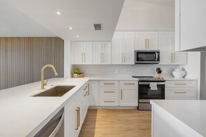 Een moderne keuken met witte kasten, gouden handgrepen, een roestvrijstalen magnetron en een inbouwoven.