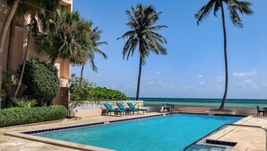A swimming pool with lounge chairs and palm trees, overlooking a beach. - GOOD VISIBILITY ~ 4 Bedroom, 3 Bathroom Condo w/ Pool and Ocean Views! (Key West)